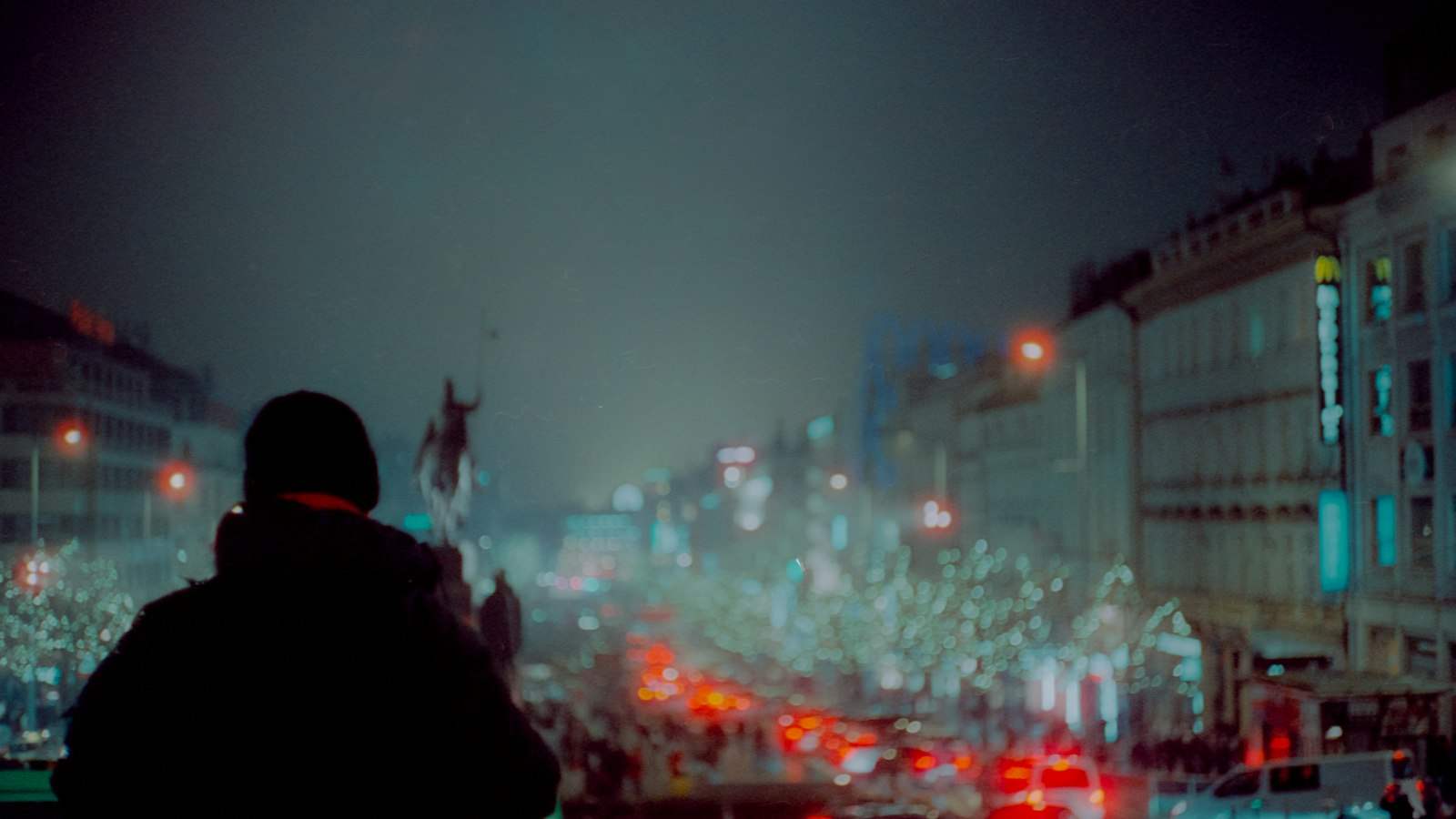 A lone figure standing in the middle of a city street at night, surrounded by blurred lights.